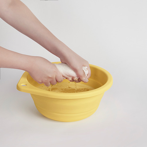 Un niño lavándose las manos en una bañera plegable de color amarillo brillante con una base texturizada para fregar.