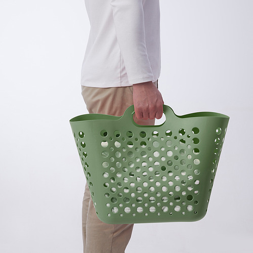Persona sosteniendo una cesta de lavandería de plástico flexible verde con asas, perfecta para llevar ropa.