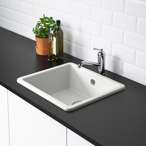 Un fregadero de cocina minimalista con un grifo cromado colocado sobre una encimera negra. El fregadero tiene esquinas redondeadas y forma parte de la serie HAVSEN.