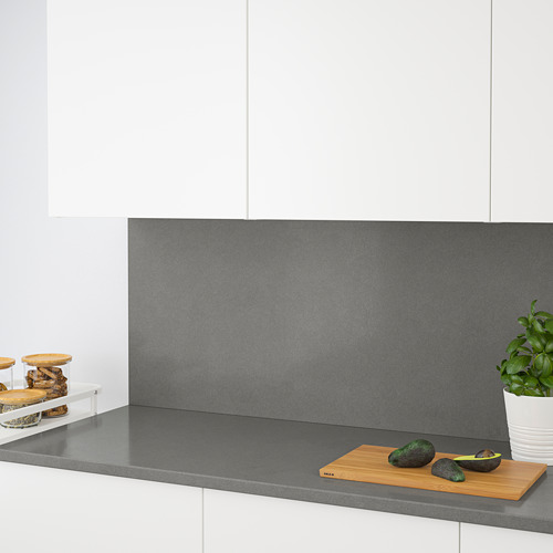 Cocina moderna con panel de pared de cuarzo, resistente a las manchas, arañazos y humedad. La encimera gris sostiene una tabla de cortar con aguacates y plantas.