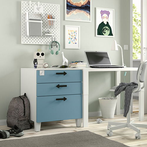 Moderna oficina en casa con escritorio blanco y azul SMÅSTAD, ordenador portátil, silla gris, obras de arte coloridas, auriculares y mochila.