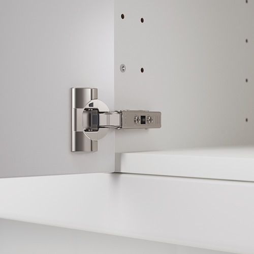 Bisagra de cocina plateada con brazos ajustables y amortiguador integrado montado sobre mueble blanco.