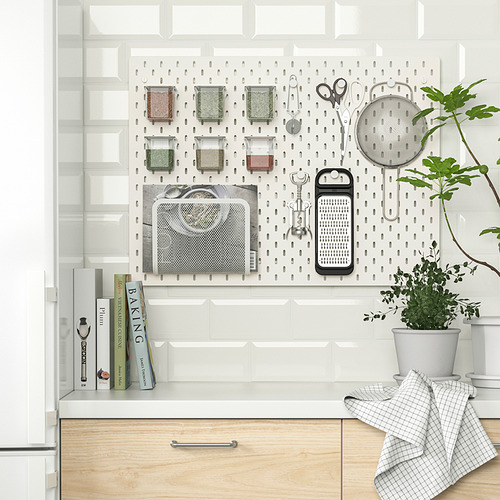 Cocina organizada con tablero perforado SKÅDIS que muestra varias especias, utensilios y libros de cocina en una pared blanca.