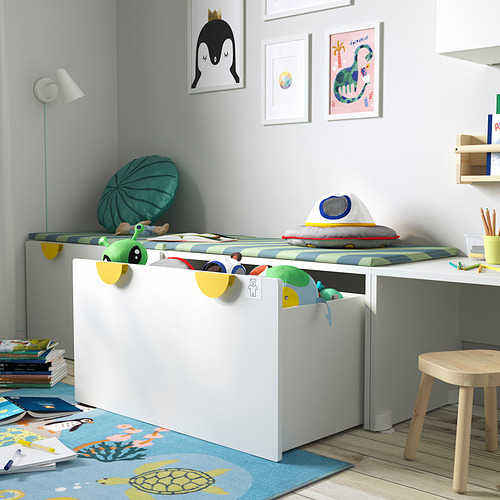 Habitación para niños con banco de almacenamiento SMÅSTAD, que sujeta los juguetes de forma ordenada. Almohadas y peluches de colores brillantes están en la parte superior.