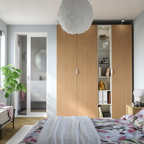 Dormitorio moderno con armario alto PAX marrón, puertas corredizas de vidrio, colcha estampada, planta y lámpara colgante.