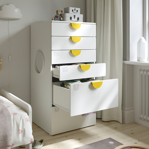 Habitación infantil con cómoda blanca, tiradores amarillos. Los cajones superiores se abren, mostrando el almacenamiento para ropa y artículos pequeños.