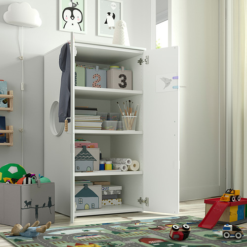 Armario blanco abierto lleno de juguetes para niños y materiales de manualidades. Las puertas están ligeramente entreabiertas.