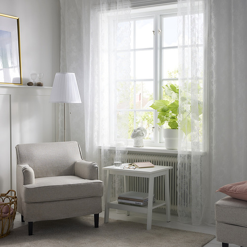 Luminoso salón con cortinas de encaje, sillón y mesa. La luz natural y el verdor visible a través de las cortinas, creando un espacio moderno y acogedor.