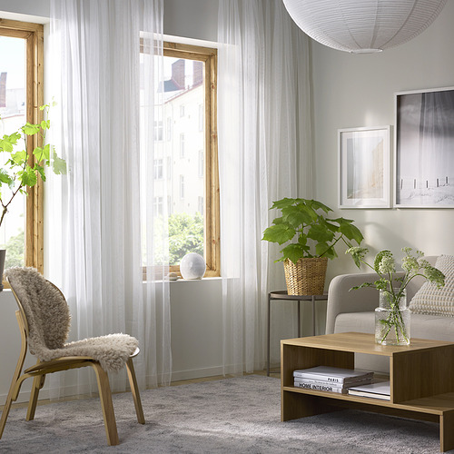 Sala de estar moderna con ventana, cortinas transparentes, silla, plantas, mesa de café y alfombra. Iluminación tenue y diseño minimalista.