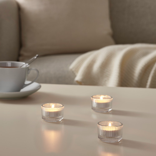 Tres velas de candelita encendidas en soportes de vidrio transparente sobre una mesa de luz, junto a una taza de café y una cuchara.