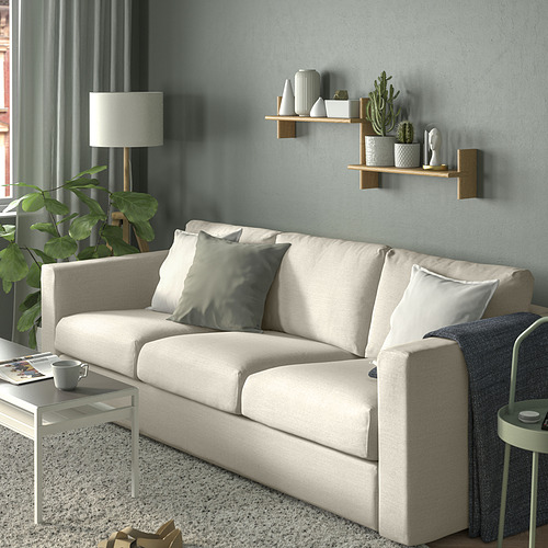 Habitación moderna con sofá KLAVRESTRÖM gris claro, almohadas blancas, estantes de madera con plantas y jarrones, cortinas grises, mesa pequeña, lámpara y alfombra.