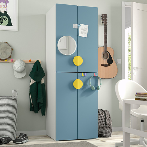 Armario SMÅSTAD azul con tiradores amarillos, espejo y bisagras de cierre suave junto a la puerta. Rodeado de una silla, una guitarra y arte mural. Compacto y espacioso.