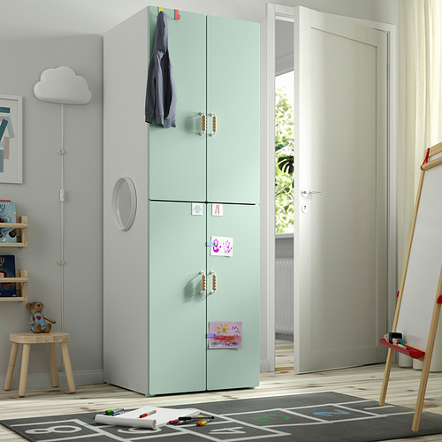 Armario infantil verde con manijas de madera cerca de la puerta, más alto que el taburete y la alfombra cercanos.