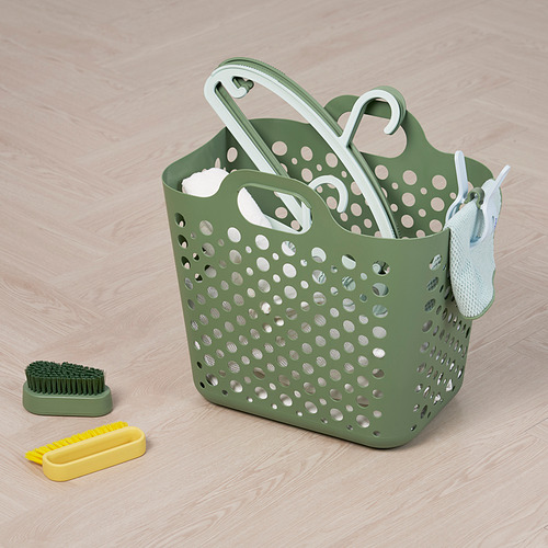 Cesta de lavandería perforada verde con asas blancas, que contiene cepillos y herramientas de limpieza, ideal para organizar y transportar la ropa.