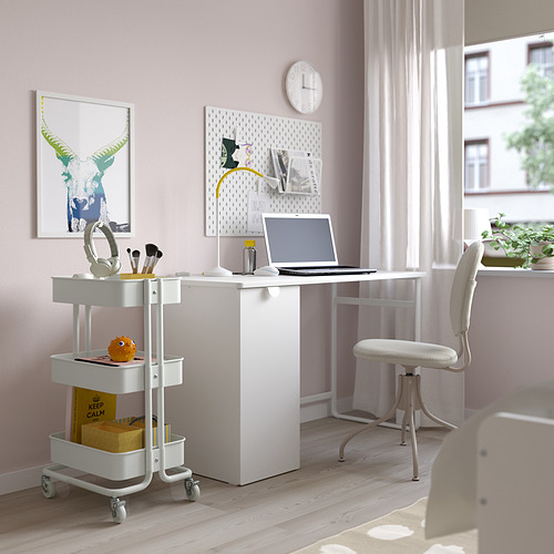 Espacio de trabajo compacto de paredes rosas con carro RÅSKOG, portátil, auriculares, taza, contenedores y tablero perforado. Iluminado por una gran ventana y una silla blanca.