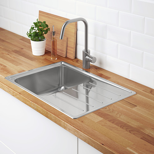 Fregadero de acero inoxidable con escurridor sobre encimera de madera, con grifo cromado moderno y planta en maceta.