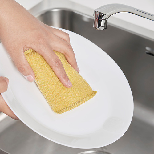 Persona limpiando un plato blanco con un estropajo amarillo debajo de un grifo cromado.