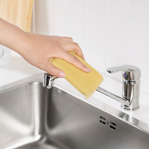Limpia a mano el grifo de la cocina con una esponja amarilla.