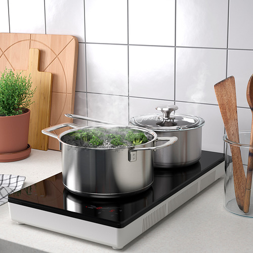 Moderna placa de inducción con dos ollas para cocinar verduras, colocadas en una elegante encimera de cocina. Controles táctiles y utiliza utensilios de cocina magnéticos.
