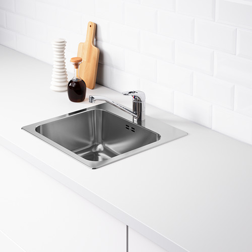 Fregadero de acero inoxidable con grifo cromado, colocado en encimera blanca. El borde trasero es más profundo para el almacenamiento.