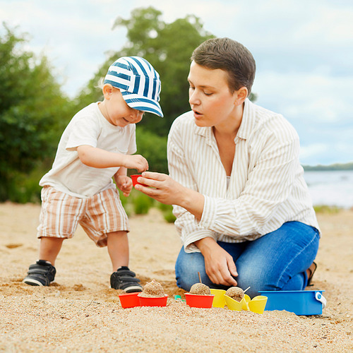 Adulto y niño juegan con moldes de arena en la playa.