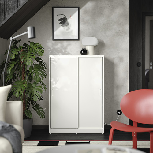 Habitación minimalista con mueble TONSTAD blanco, silla roja, gran planta verde, arte en blanco y negro y lámpara blanca.