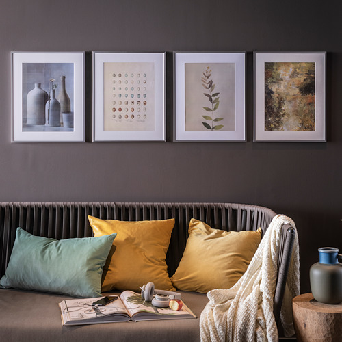 Cuatro obras de arte enmarcadas sobre el sofá con almohadas amarillas / verdes, manta blanca, libro y jarrón con frutas.