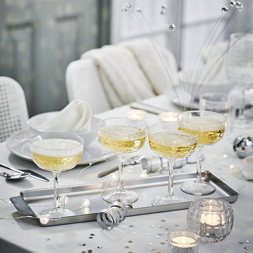 Elegante mesa con cuatro copas de vino, platos y cubiertos de plata. El centro tiene un pequeño portavelas transparente y decoraciones de estrellas.