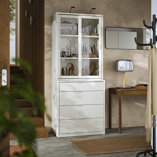 Armario y arcón TONSTAD blanco roto, puertas de cristal, suelo de madera, pared gris, lámpara beige.