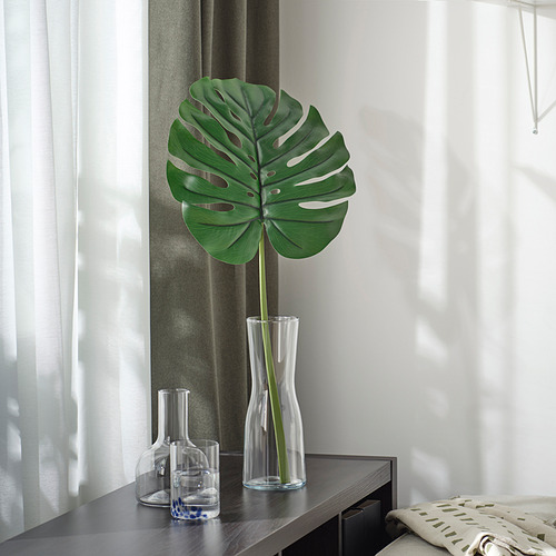 Gran hoja verde artificial en jarrón de vidrio transparente en un estante oscuro, con dos recipientes de vidrio más pequeños; Decoración moderna.