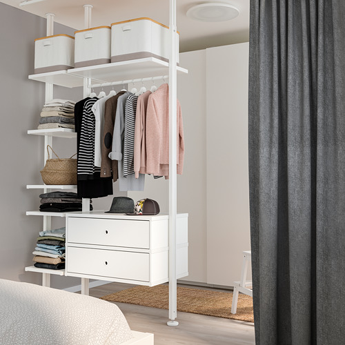 Armario ELVARLI blanco con ropa, cajones, estantes y cortina gris en un dormitorio ordenado.