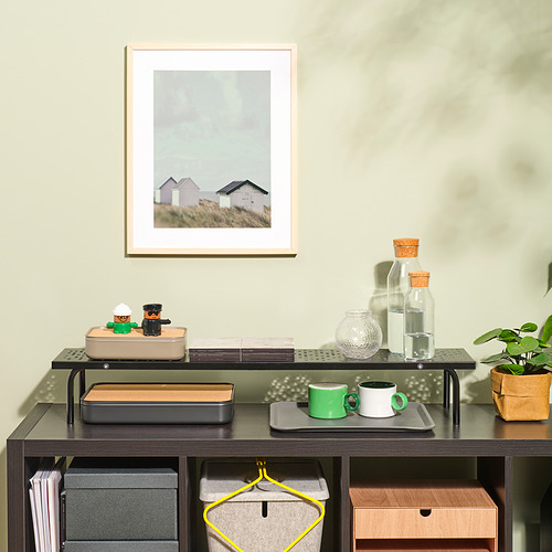 Escritorio con soporte para monitor, estantes con tazas y libros, foto enmarcada y planta.