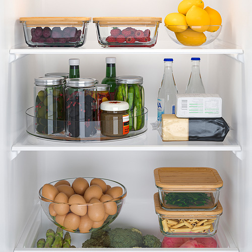 Nevera organizada con plato giratorio con encurtidos, queso, botellas. Frutas y verduras en envases de vidrio.