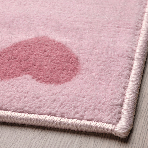 Primer plano de una alfombra rosa suave y afelpada con un delicado patrón de corazón, bordeada con una trenza retorcida.