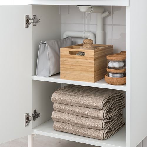 Mueble de baño blanco con toallas dobladas, caja de madera y organizador de corcho.