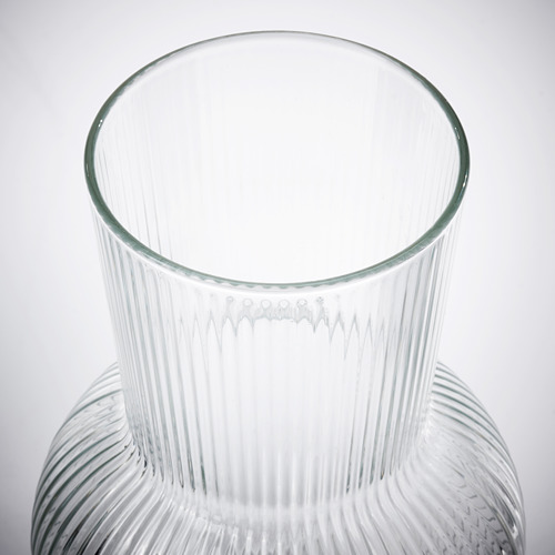 Jarrón de vidrio transparente con nervaduras verticales, reflejando la luz, elegante y refinado.