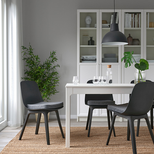 Acogedora configuración de comedor con almohadilla de silla gris, cerca de la estantería, lámpara de luz cálida.