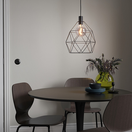 Comedor moderno con lámpara BRUNSTA, pequeña mesa oscura, sillas de madera, jarrón verde con flores y platos azules.