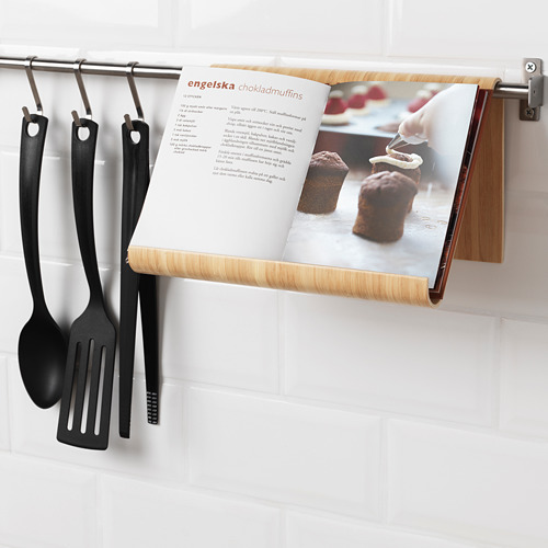 Soporte para libros de cocina montado en la barra de la cocina, que sostiene la página de recetas abierta con muffins de chocolate. Tres utensilios de cocina negros cuelgan a su lado.