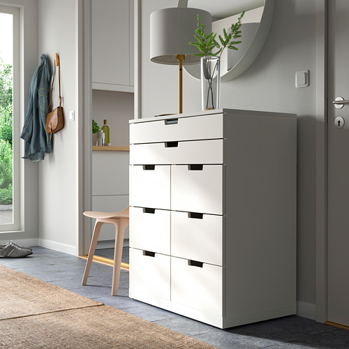 Cómoda NORDLI blanca moderna con seis cajones, alta, elegante, junto a la puerta, cerca de los percheros y el taburete.