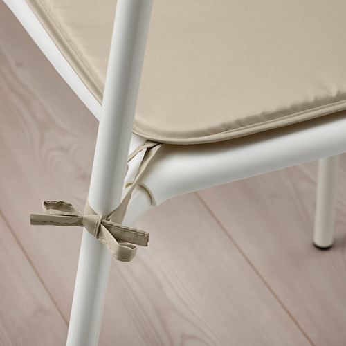 Cojín de silla BRÄMÖN beige asegurado a patas blancas. Tejido de dos caras repelente al agua para interiores y exteriores.