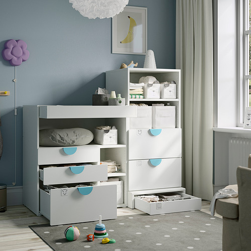 Una habitación para bebés con cajones de almacenamiento blancos, detalles en azul y una alfombra gris con puntos blancos que evita resbalones.