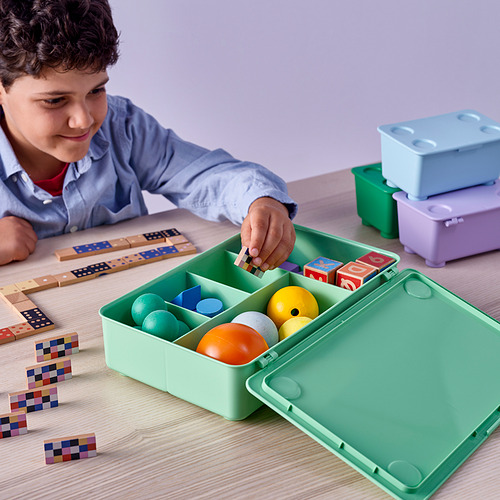 Niño jugando con bloques cerca de una caja verde de GLIS con juguetes adentro.