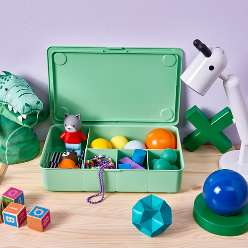 Caja de almacenamiento de plástico verde llena de bolas de colores, un gato de juguete y un peluche de lagarto; se asienta sobre una superficie de madera.