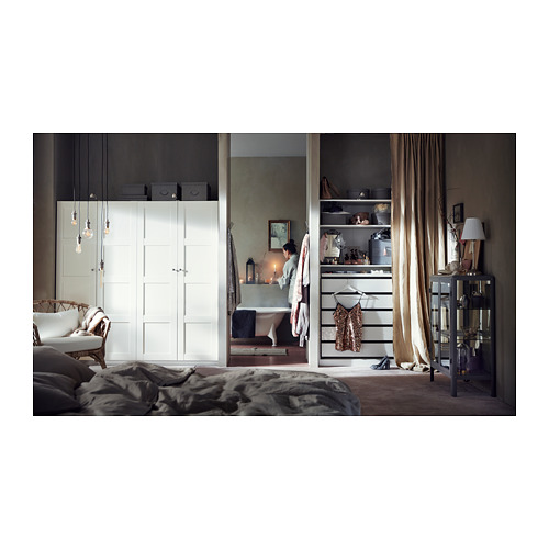 Dormitorio moderno con armarios blancos, lámparas colgantes, cortinas beige. Cama deshecha a la izquierda, bañera independiente en el centro con una mujer al lado.