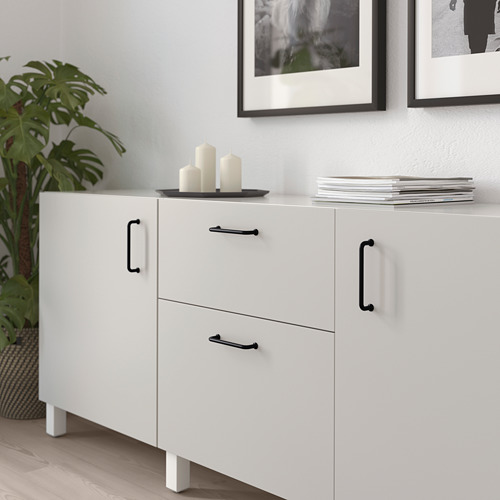 Mueble blanco con asas negras, donde se exhiben velas, libros y plantas.