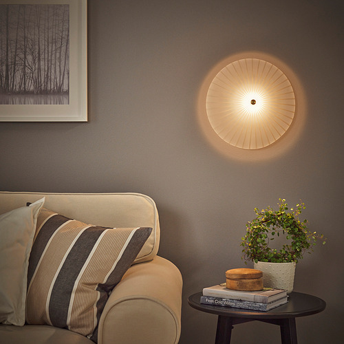 Moderno salón con lámpara de pared RORKULT sobre un sofá beige, mesa de centro con plantas, libros y decoración. La pared gris oscuro contrasta con el cálido resplandor de las lámparas.
