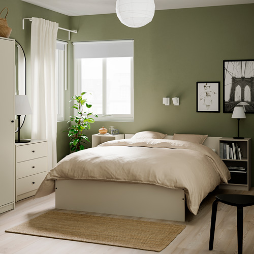 Dormitorio moderno con armario verde GURSKEN, cama blanca, suelo de madera y arte de pared. Armario alto, a juego con la mesita de noche.