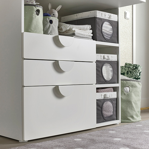 Mueble de almacenaje blanco con cajones, cajas grises con ventanas de malla y un peluche. Se utiliza para organizar artículos para bebés.