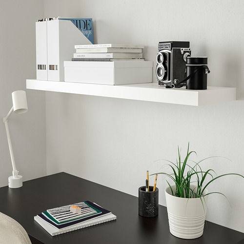 Estante blanco LACK con libros y cámara sobre mesa oscura y lámpara.